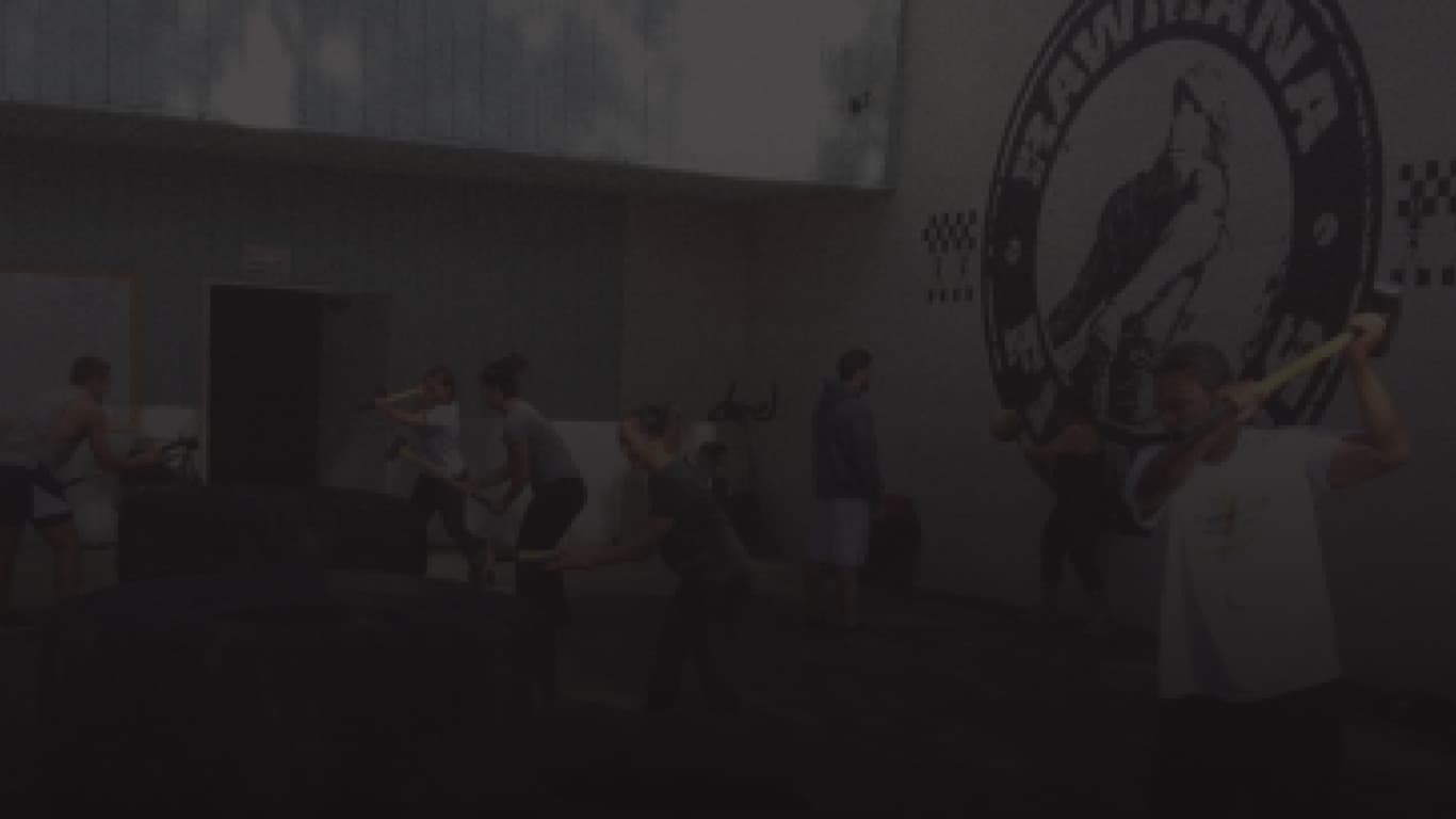 Members training with barbells beneath the Rawmana Fitness wall logo.